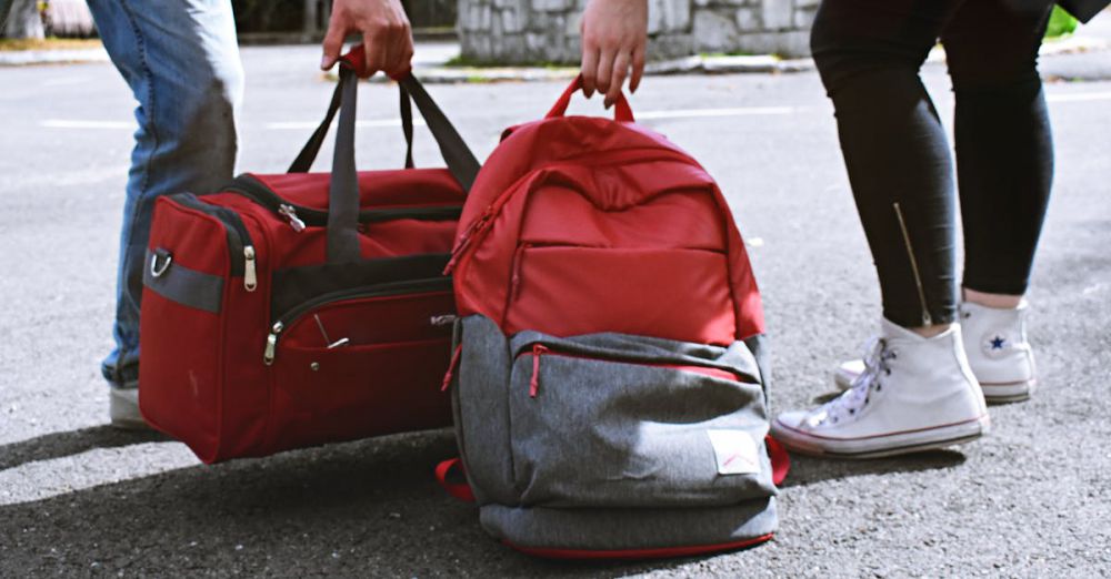 Duffel Bags - Two travelers holding red bags on a street, symbolizing travel and exploration.