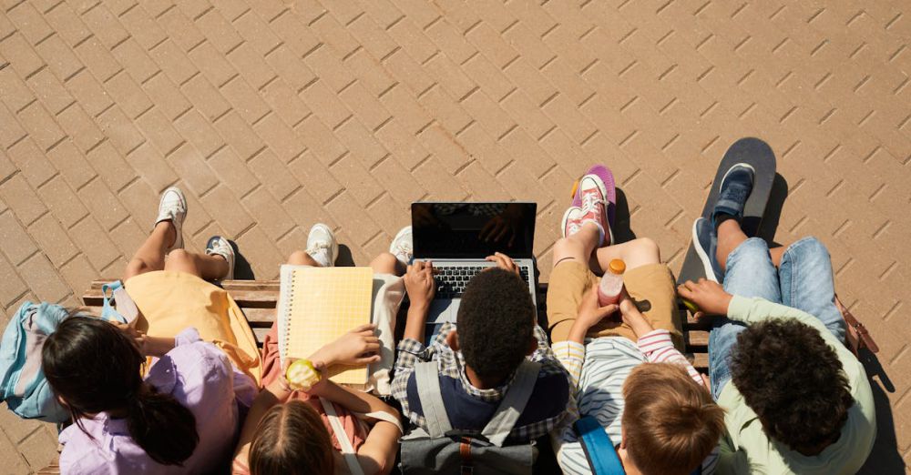 Laptop Backpacks - Group of teenagers sitting on a bench with a laptop, enjoying a sunny day outdoors.