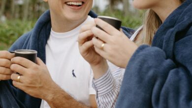 Travel Blankets - Happy couple enjoying coffee wrapped in blankets amidst tropical palm trees.