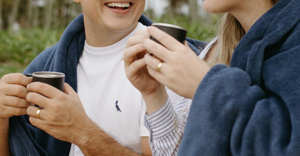 Travel Blankets - Happy couple enjoying coffee wrapped in blankets amidst tropical palm trees.