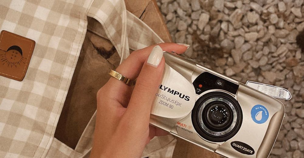 Travel Essentials - Close-up of hand holding a vintage film camera with a checkered bag on a wooden surface.