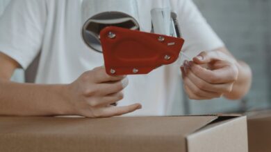 Luggage Covers - Close-up of person sealing a cardboard box with tape for packaging and shipping.