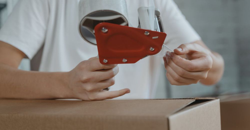 Luggage Covers - Close-up of person sealing a cardboard box with tape for packaging and shipping.