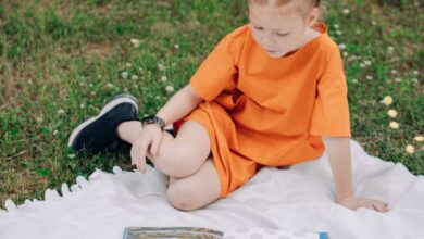 Storybooks - A child in an orange outfit reading books outdoors on a blanket. Perfect for education and leisure themes.