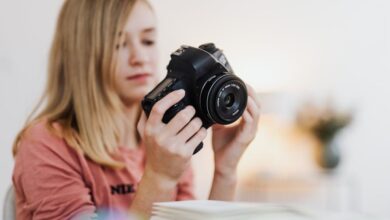 Beginner Books - Young woman examining a DSLR camera indoors with a blurred background.