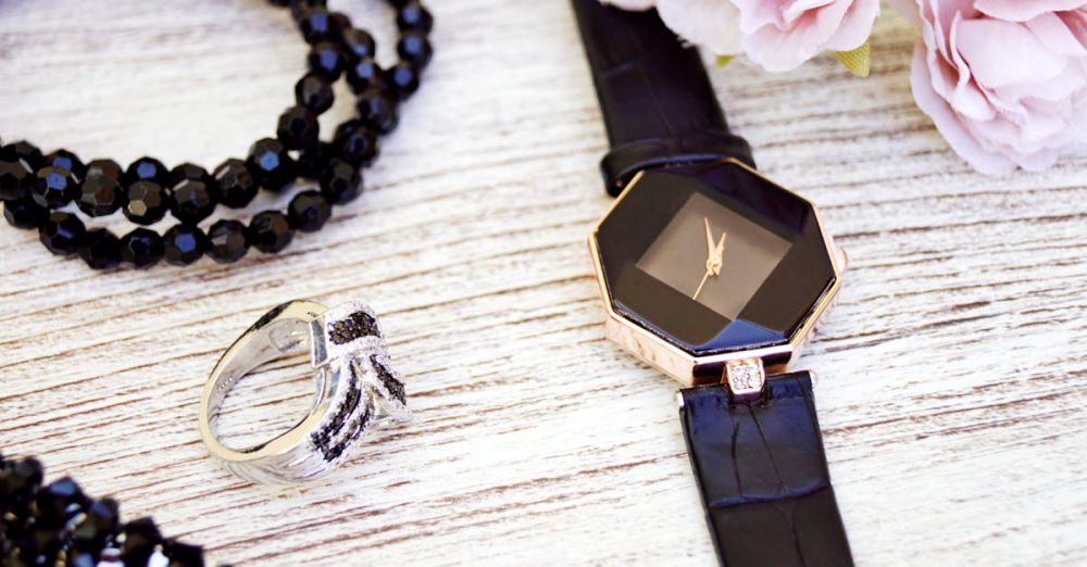 Accessories - Close-up of luxurious black jewelry and watch with pink flowers on a wooden surface.