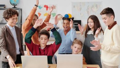 Geography Books - A group of happy students and a teacher clapping together in a school classroom.