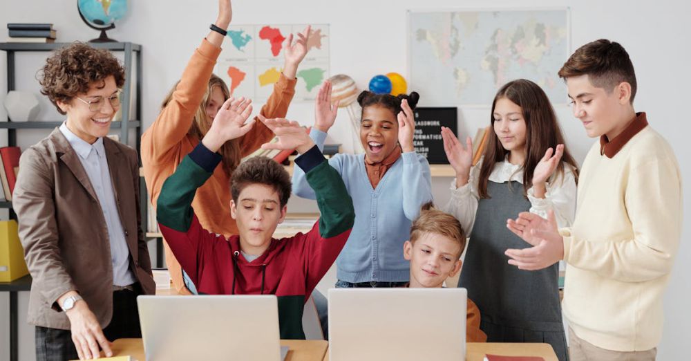 Geography Books - A group of happy students and a teacher clapping together in a school classroom.