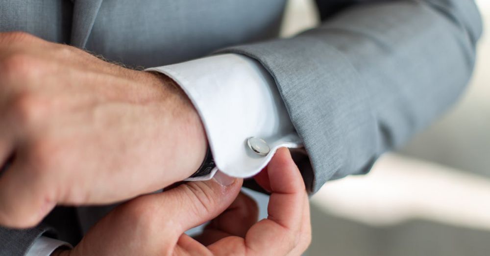 Cufflinks - Close-up of a man's hands adjusting his cufflinks on a gray suit sleeve, showcasing elegance.