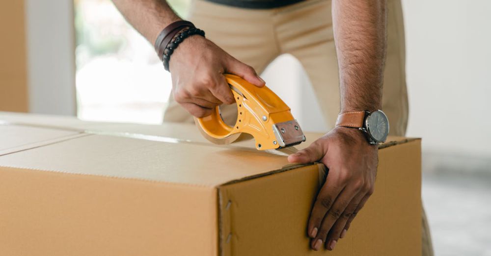 Watch Storage - Crop faceless young male with wristwatch using adhesive tape while preparing cardboard box for transportation