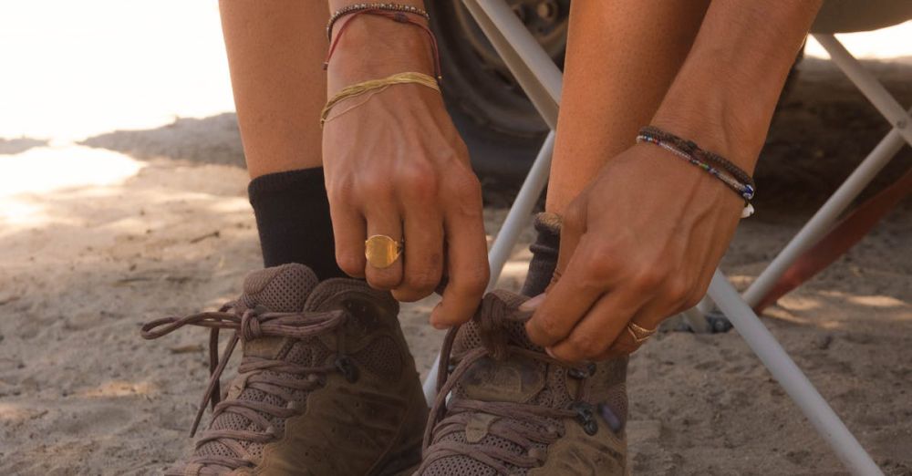 Ankle Bracelets - Close-up of an adult tying shoelaces on hiking boots while seated outdoors on a sunny day.