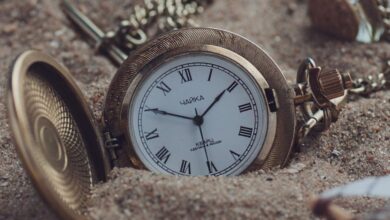 Time Zone Watches - A classic gold pocket watch partially buried in sand, exuding timeless elegance and a sense of nostalgia.