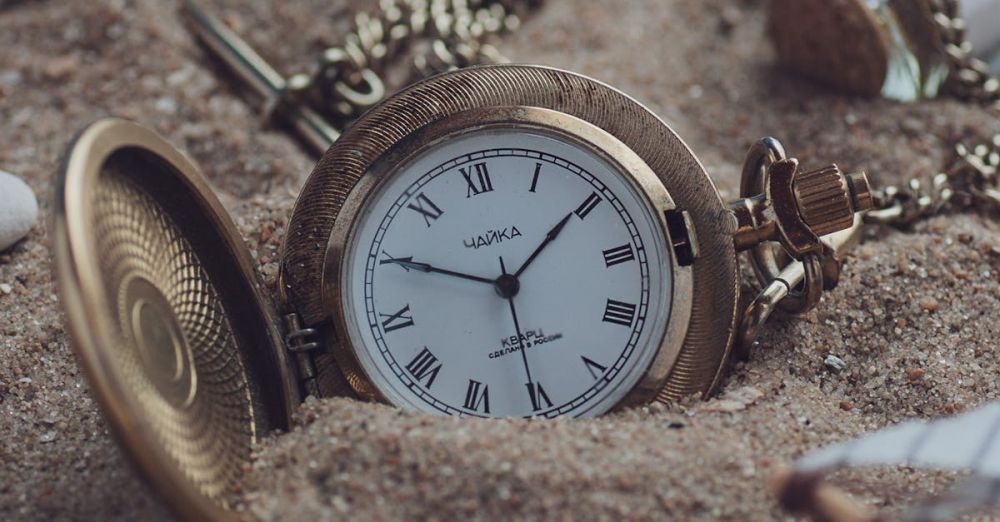 Time Zone Watches - A classic gold pocket watch partially buried in sand, exuding timeless elegance and a sense of nostalgia.