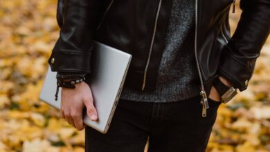 Men’s Bracelets - A person in a black leather jacket, holding a laptop, stands among fallen autumn leaves.