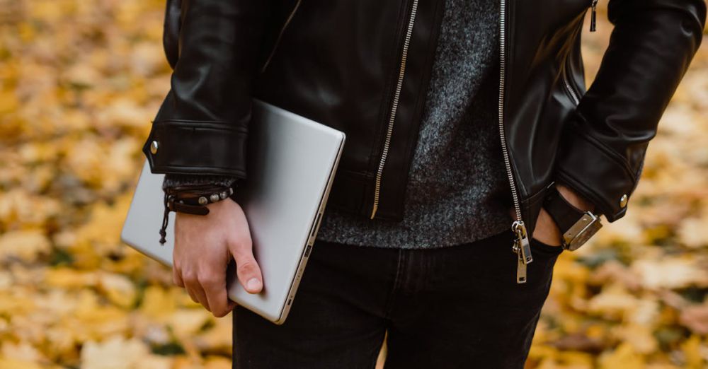 Men’s Bracelets - A person in a black leather jacket, holding a laptop, stands among fallen autumn leaves.